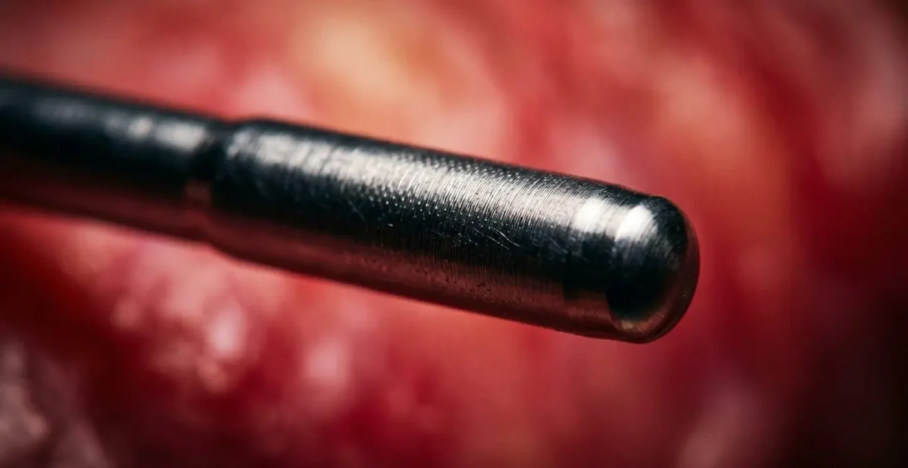 An extreme close-up of a catheter tip, showing its metallic texture against an abstract red background representing cardiac tissue.