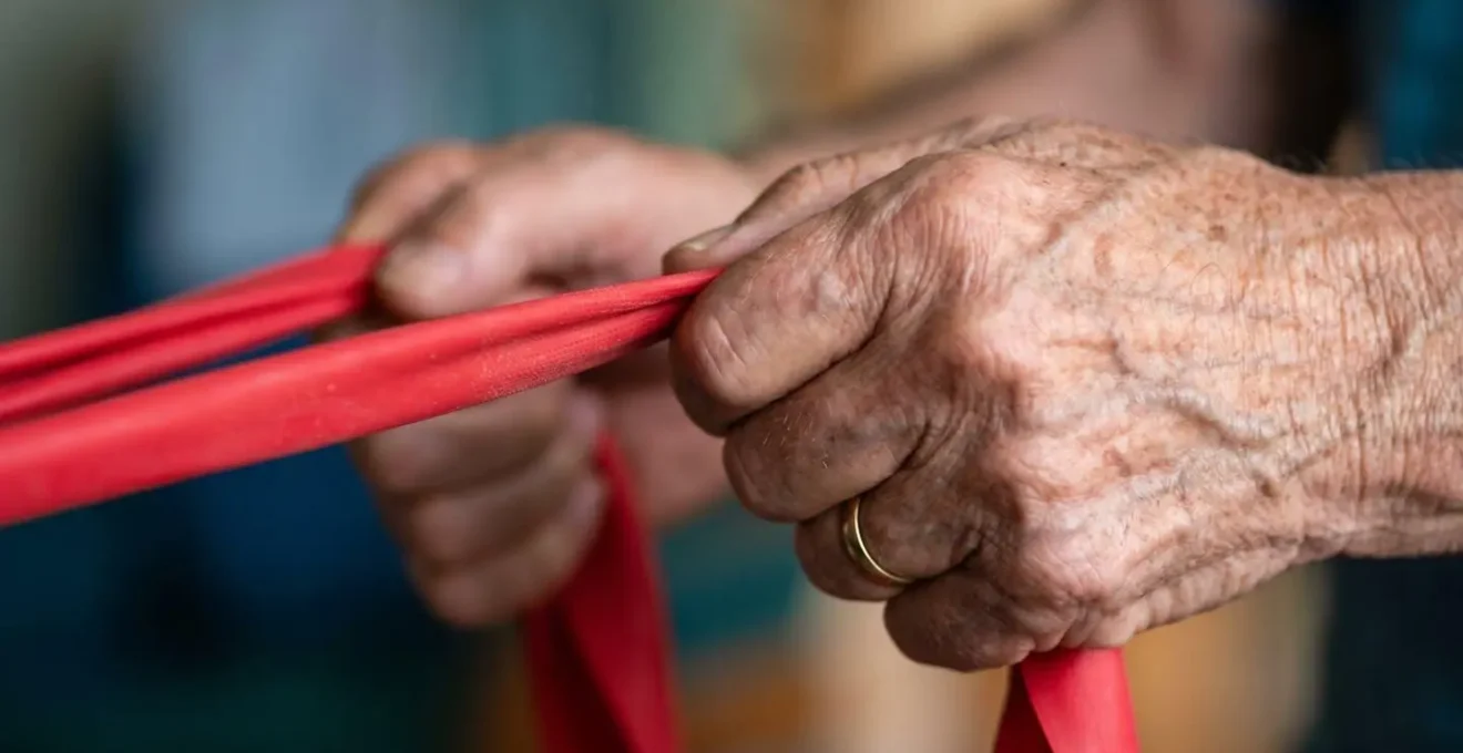 Close-up of elderly hands gripping a colorful resistance band during strength training exercise.